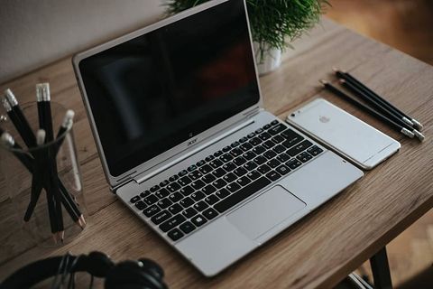 银色宏碁笔记本电脑放在一张木桌子上，上面有一株绿色植物、铅笔和一部苹果iPhone