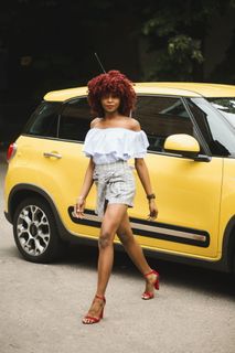 身穿白色露肩上衣的女子站在黄色菲亚特500l旁边