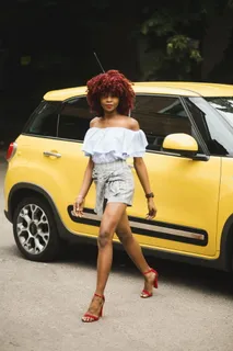 身穿白色露肩上衣的女子站在黄色菲亚特500l旁边