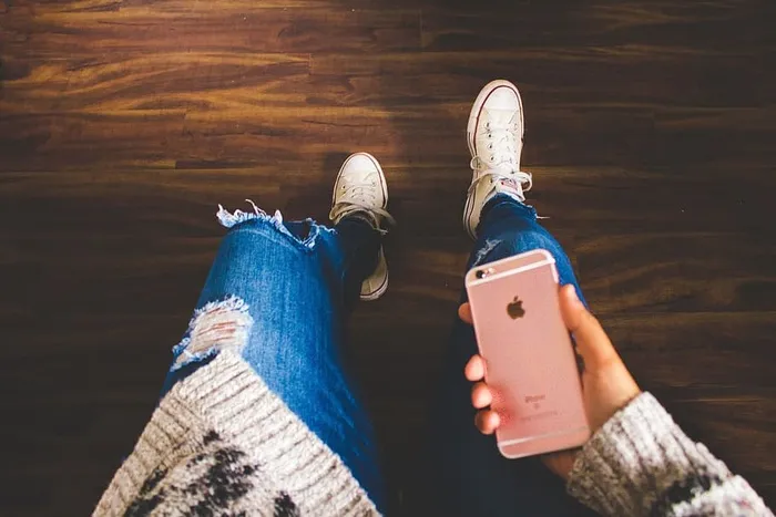一个穿着牛仔裤的女孩低头看着她的iPhone手机
