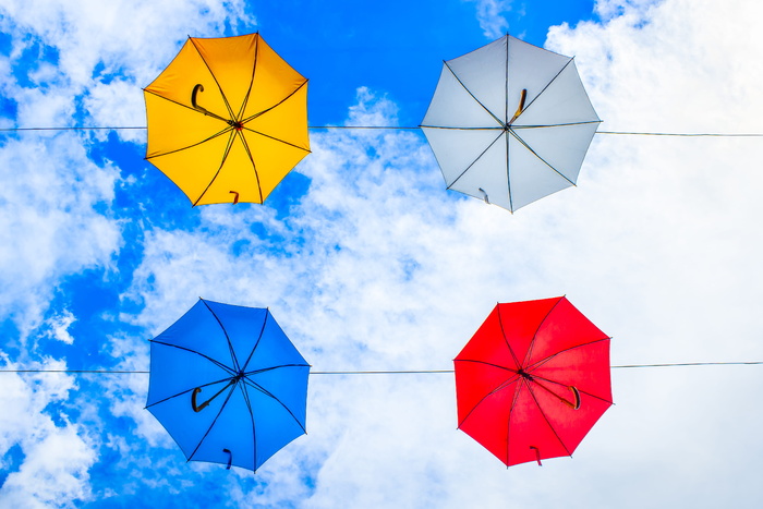 多云的天空下挂在电缆上的四把五颜六色的雨伞