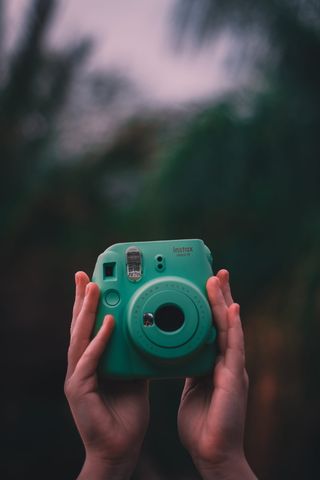 拿着teal Fujifilm Instax即时相机的人的选择性聚焦照片