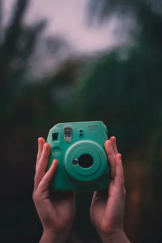 拿着teal Fujifilm Instax即时相机的人的选择性聚焦照片