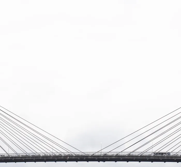 白天多云天空下灰色吊桥上的车辆