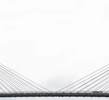 白天多云天空下灰色吊桥上的车辆