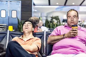 男人做鬼脸坐在躺椅上睡觉的男人旁边