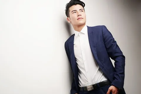 身穿蓝色上衣和白色衬衫的男子倚在白色墙壁上 身穿蓝色上衣和白色衬衫的男子倚在白色墙壁上