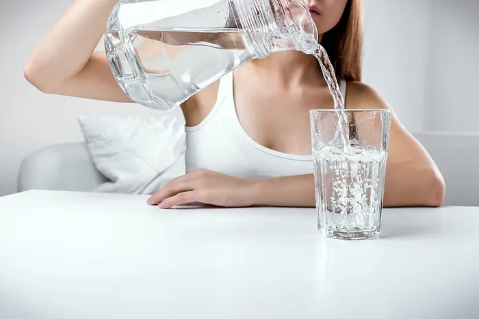 特写镜头：年轻女孩从水罐里往玻璃杯里倒清水