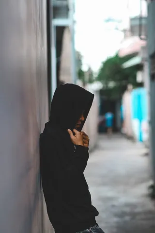 穿着黑色连帽夹克靠在墙上的人