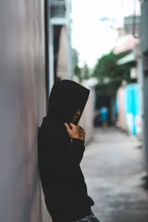 穿着黑色连帽夹克靠在墙上的人 穿着黑色连帽夹克靠在墙上的人