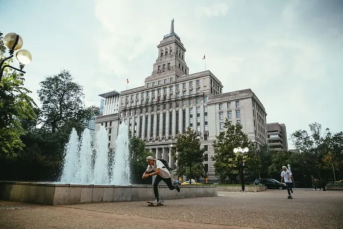年轻的高加索滑板运动员经过一座建筑物前的喷泉