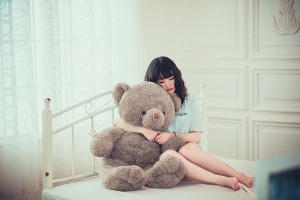 在白色床垫上拥抱灰熊毛绒玩具的女人