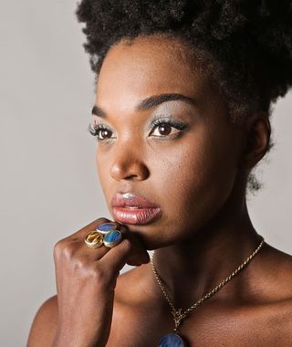 一位年轻的非洲女性戴着珠宝在室内摆好姿势，手指放在下巴上