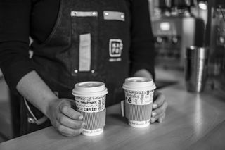 拿着一次性杯子的人的灰度照片