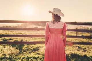 一位身穿粉色连衣裙、头戴白色帽子的女子面对绿色草地的照片