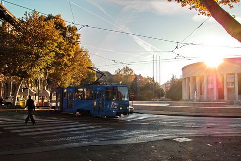 日落时，身穿黑色服装的人在蓝色有轨电车附近的人行道上行走