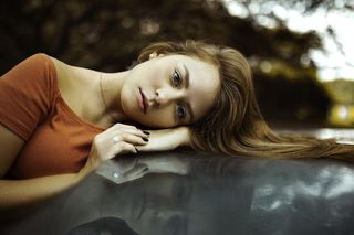 身穿橙色上衣的女子倚在车顶上