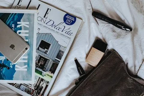 白色床单上的银色笔记本电脑、相机、杂志和其他物品