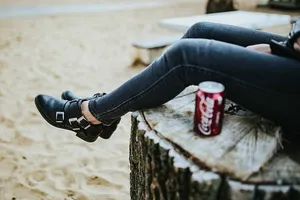 美丽的金发女人在海滩边的树桩上拿着一罐可乐放松
