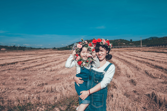 女孩抱着蹒跚学步的孩子，手持花圈在田野上