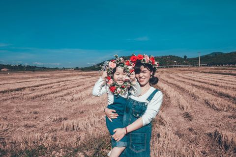 女孩抱着蹒跚学步的孩子，手持花圈在田野上