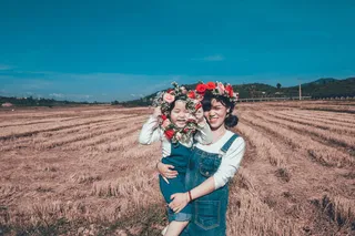 女孩抱着蹒跚学步的孩子，手持花圈在田野上