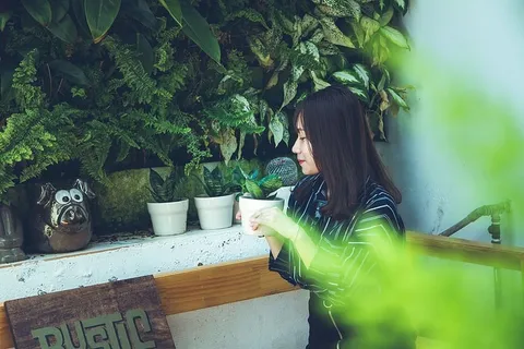 坐在白色墙壁附近的一位妇女，手里拿着一个白色的陶罐，里面有绿色的植物