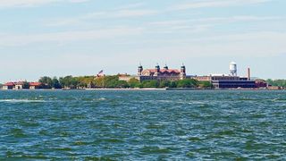 在纽约港周围一个美丽的夏日，埃利斯岛笼罩在云层覆盖的天空下。