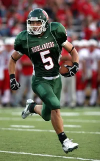 身穿绿色美式橄榄球球衣的男子在球场上跑步时持球