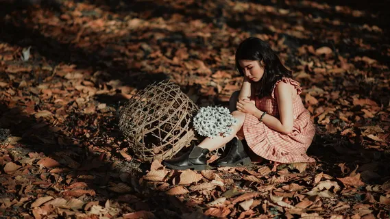 穿着红色连衣裙的女人坐在棕色的地上，带着编织的棕色篮子