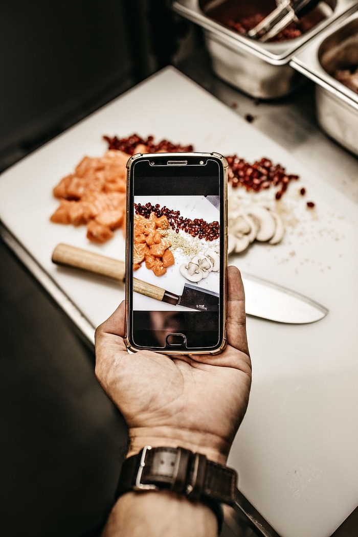 手持智能手机拍摄熟食照片的人