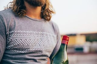 一个留着胡子的白人男子穿着T恤，手里拿着一个意大利瓶子