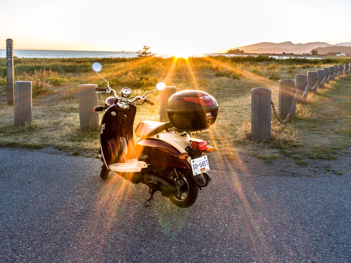 停在灰色道路上的带黑色顶箱的栗色摩托车
