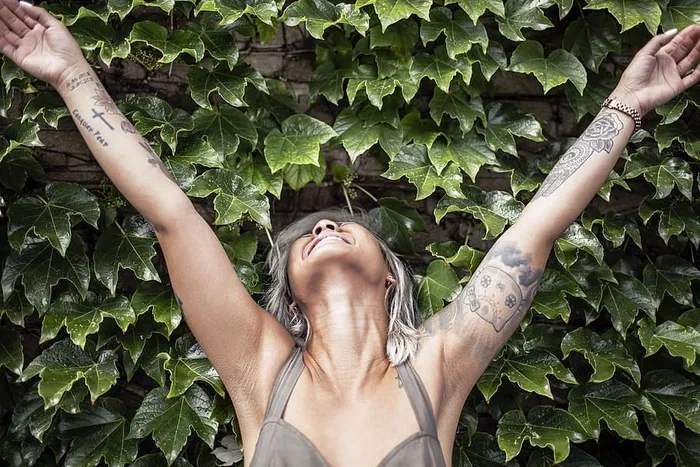 一名女子穿着带有手臂纹身的吊带上衣，举起双手