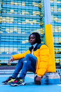 一名身穿黄黑色拉链泡泡夹克的男子坐在金属柱旁