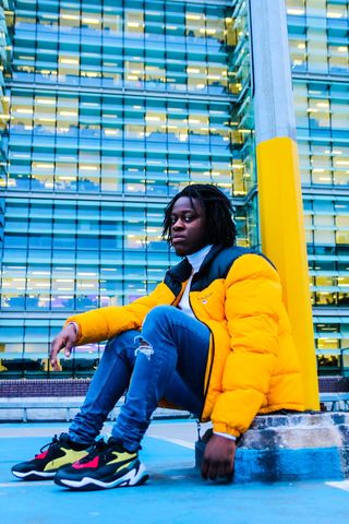 一名身穿黄黑色拉链泡泡夹克的男子坐在金属柱旁