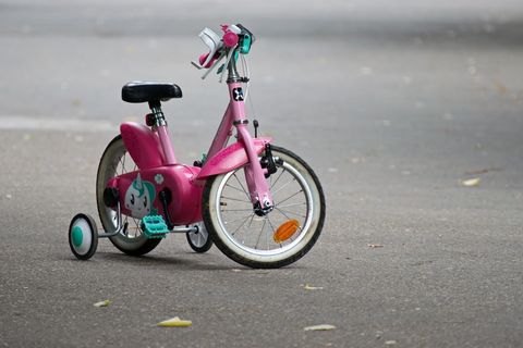灰色路面上带训练轮的粉红色自行车