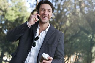 一个穿着灰色外套的白人青年在户外打电话