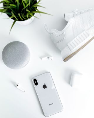 银色iPhone X近白色阿迪达斯NMD鞋、带外壳的AirPods和粉笔谷歌Home Mini