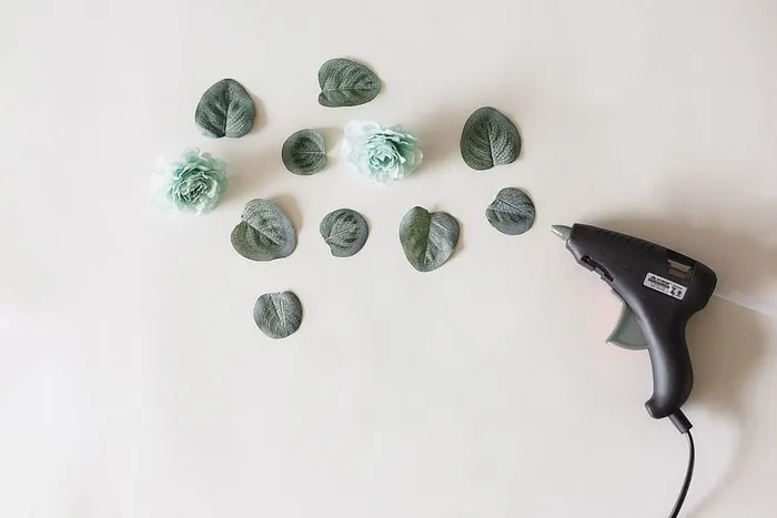 在白色表面上的绿叶和花朵旁边使用胶水枪