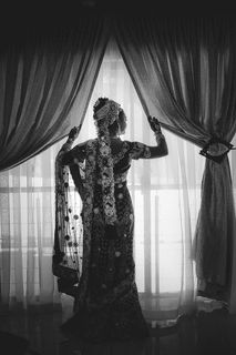 身着白色透明连衣裙的女子站在窗前的灰度照片