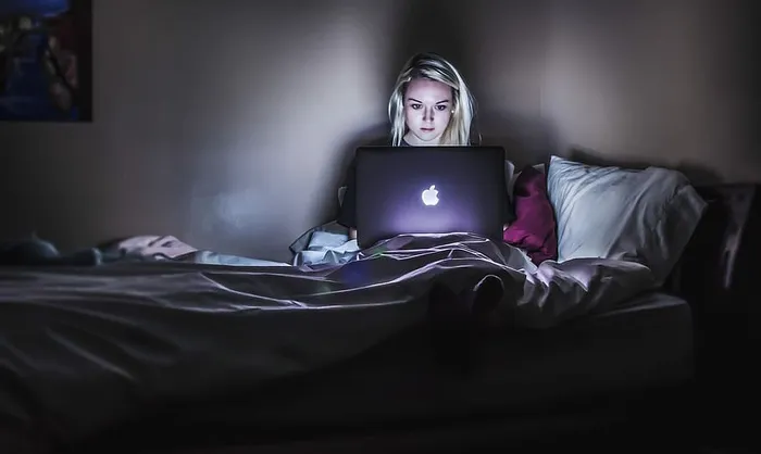坐在床上，膝盖上放着MacBook的女人