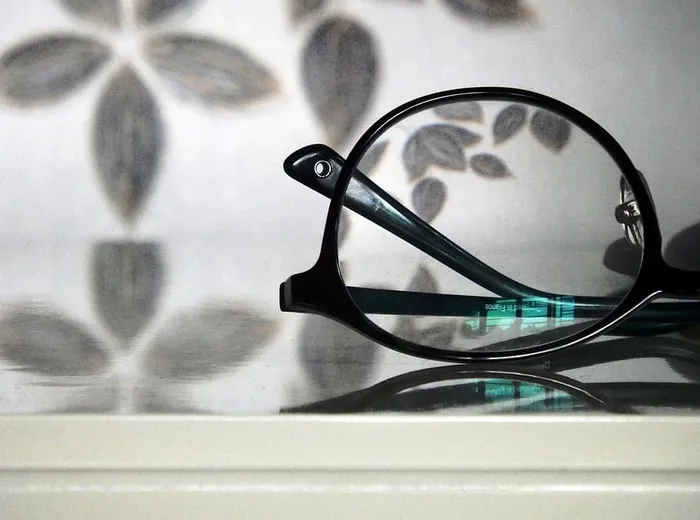 一副黑框眼镜的抽象视图，背景为花卉图案，镜片中反射着绿松石色光线
