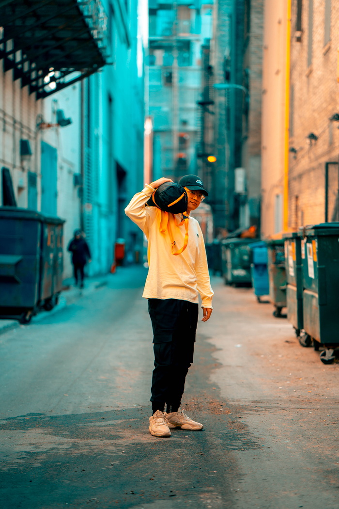 一名身穿白色长袖衬衫和黑色长裤的男子手持吊杆盒站在巷子上