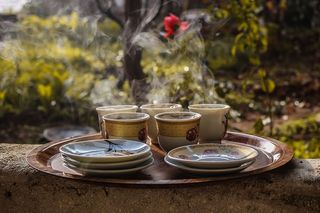 茶托旁边的棕色陶瓷茶杯放在棕色盘子上