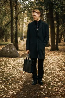 男子手持手提包站在绿树下