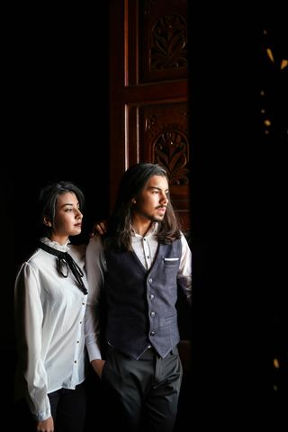 身穿灰色背心的男子站在穿着白色衬衫的女子旁边