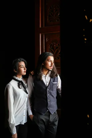 身穿灰色背心的男子站在穿着白色衬衫的女子旁边