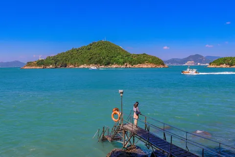 在蓝天下，站在面向大海的木质码头上的女人