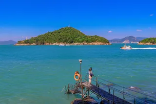 在蓝天下，站在面向大海的木质码头上的女人